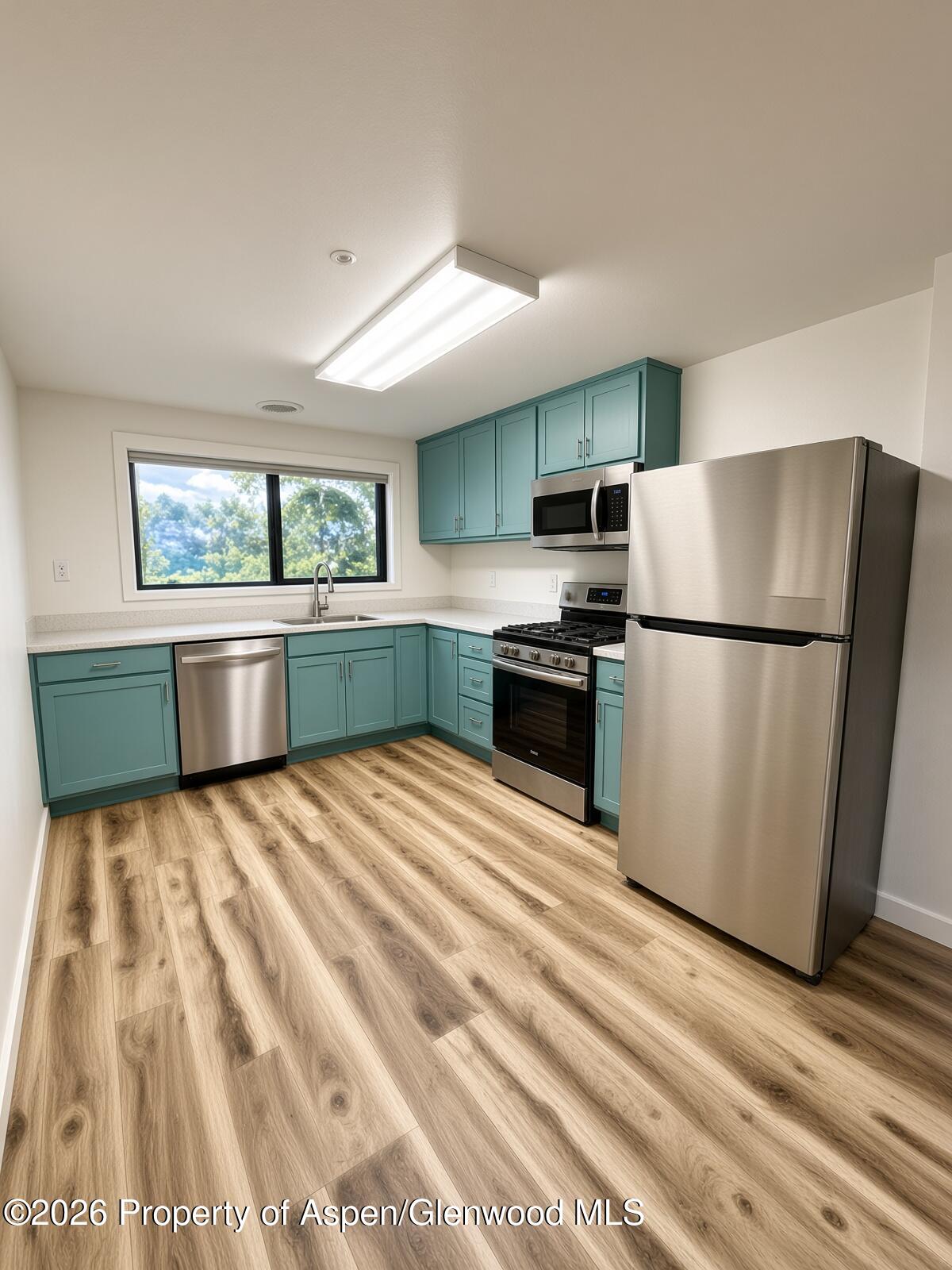 Kitchen with teal cabinetry, stainless steel appliances, and wood-look plank flooring.