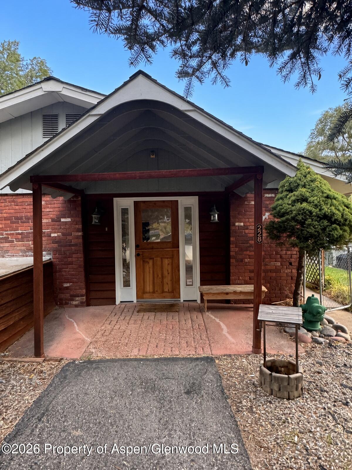 Home entrance with brick walls, a peaked covered porch, and a wooden front door.