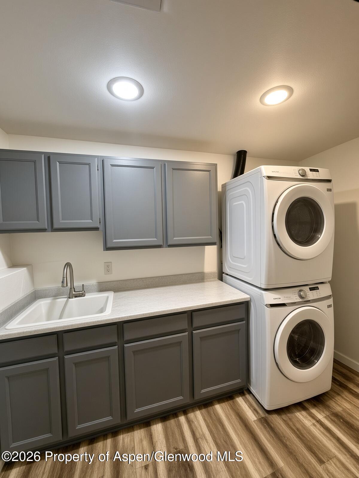 Laundry room with gray cabinets, a utility sink, and a stacked washer and dryer.