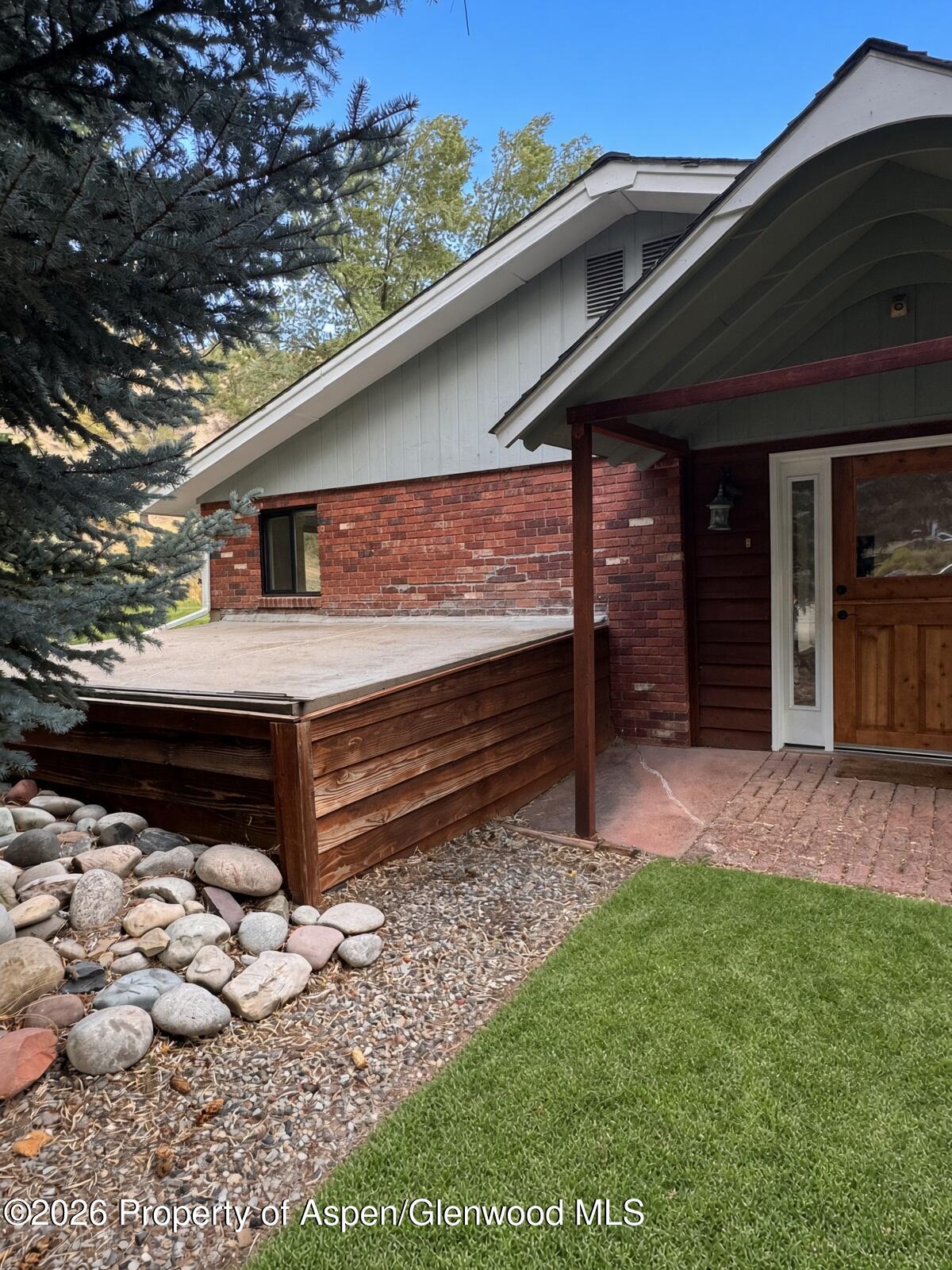 Home entrance with a covered porch, wooden front door, raised platform, and river-rock landscaping.