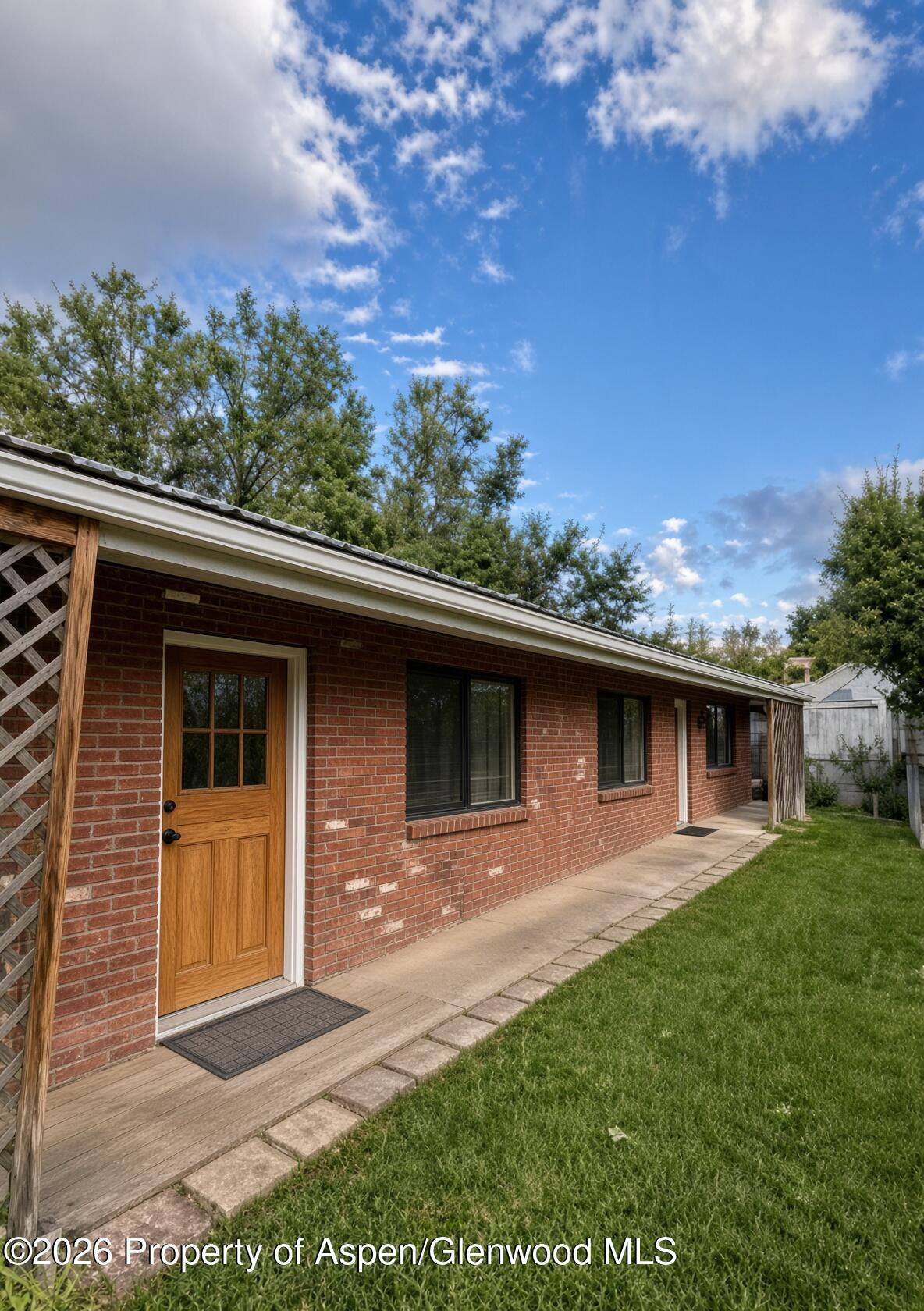 Red brick home with a wooden entry door, long side walkway, and grassy yard.