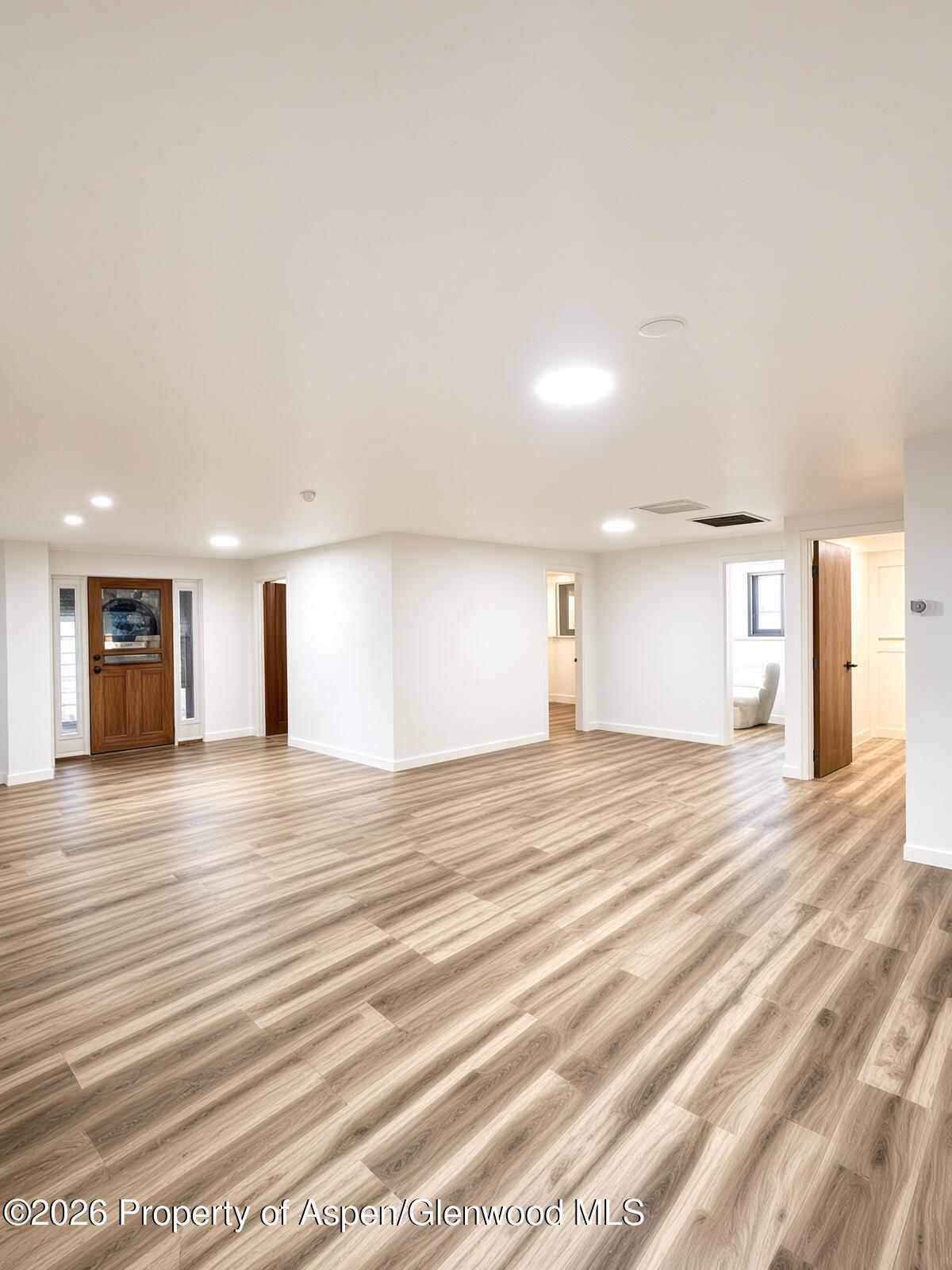Open interior with wood-look plank flooring, recessed lights, and a wooden entry door.