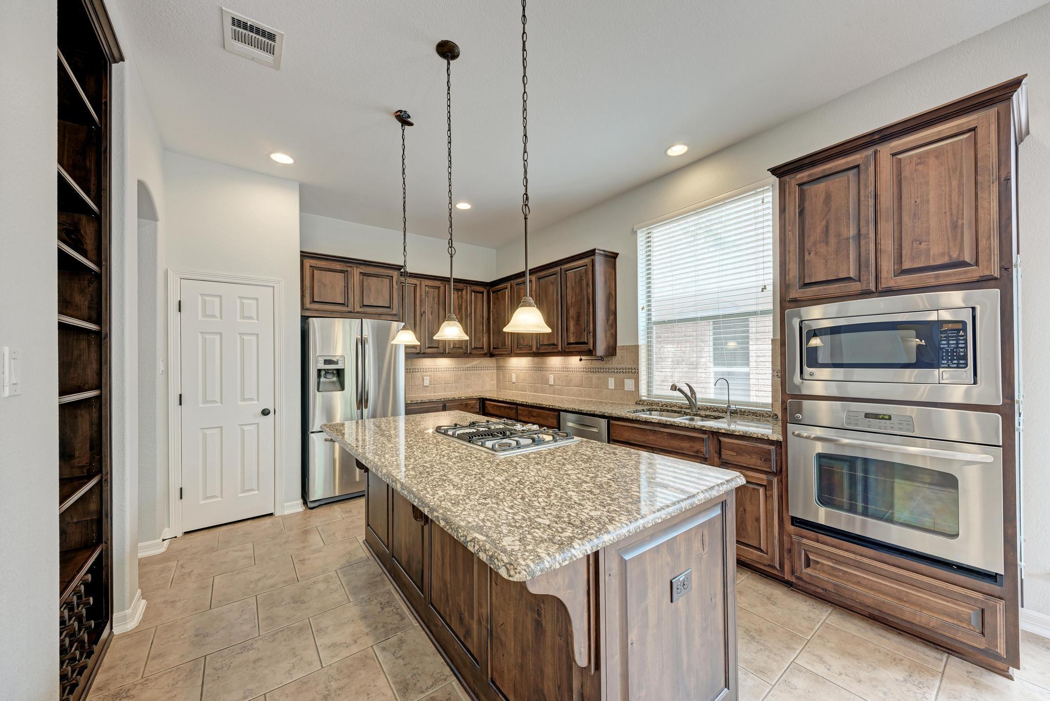 Kitchen with dark wood cabinetry, granite cooktop island, and stainless steel appliances.