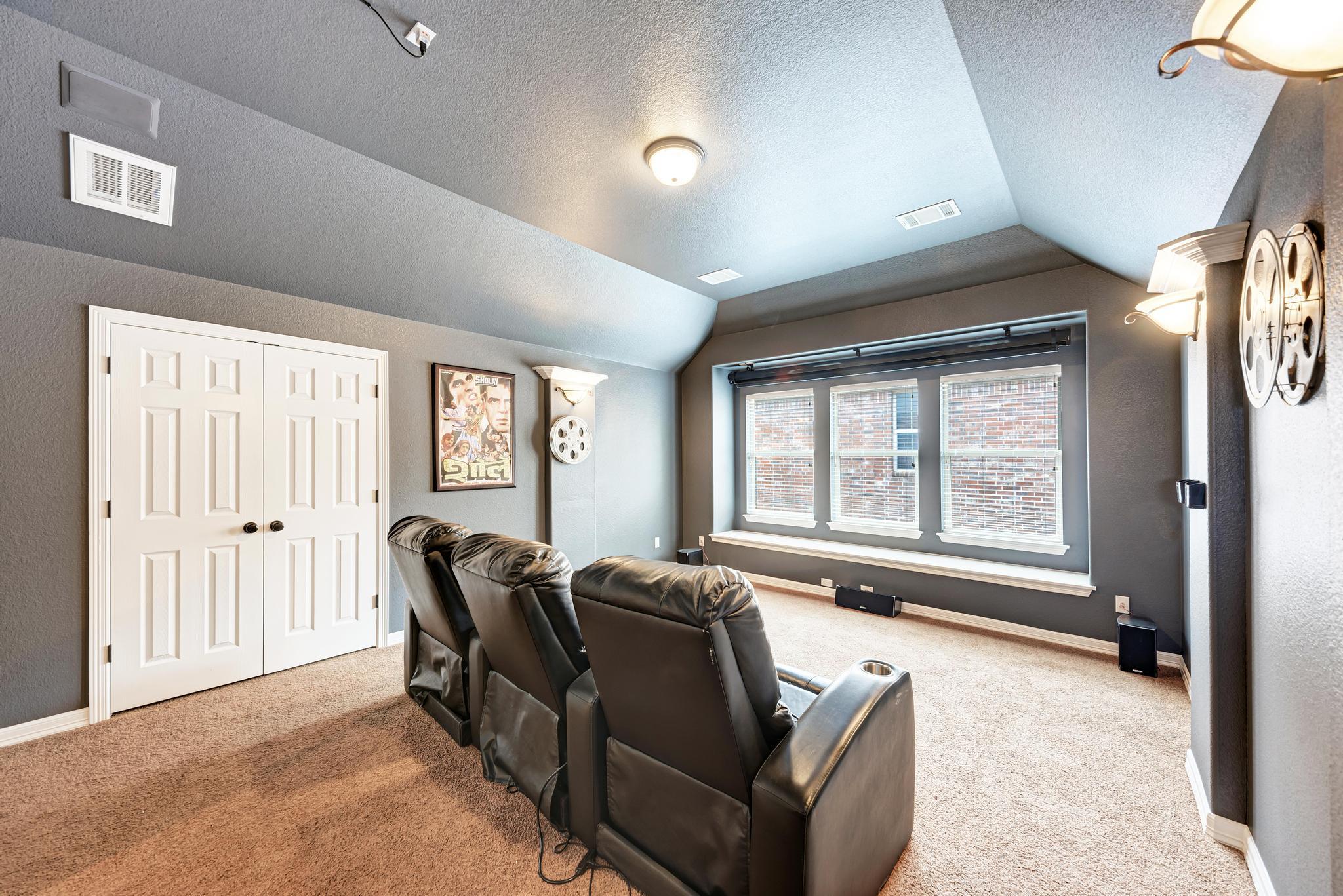 Home theater with dark leather recliners, three windows, carpet, and film-themed wall decor.