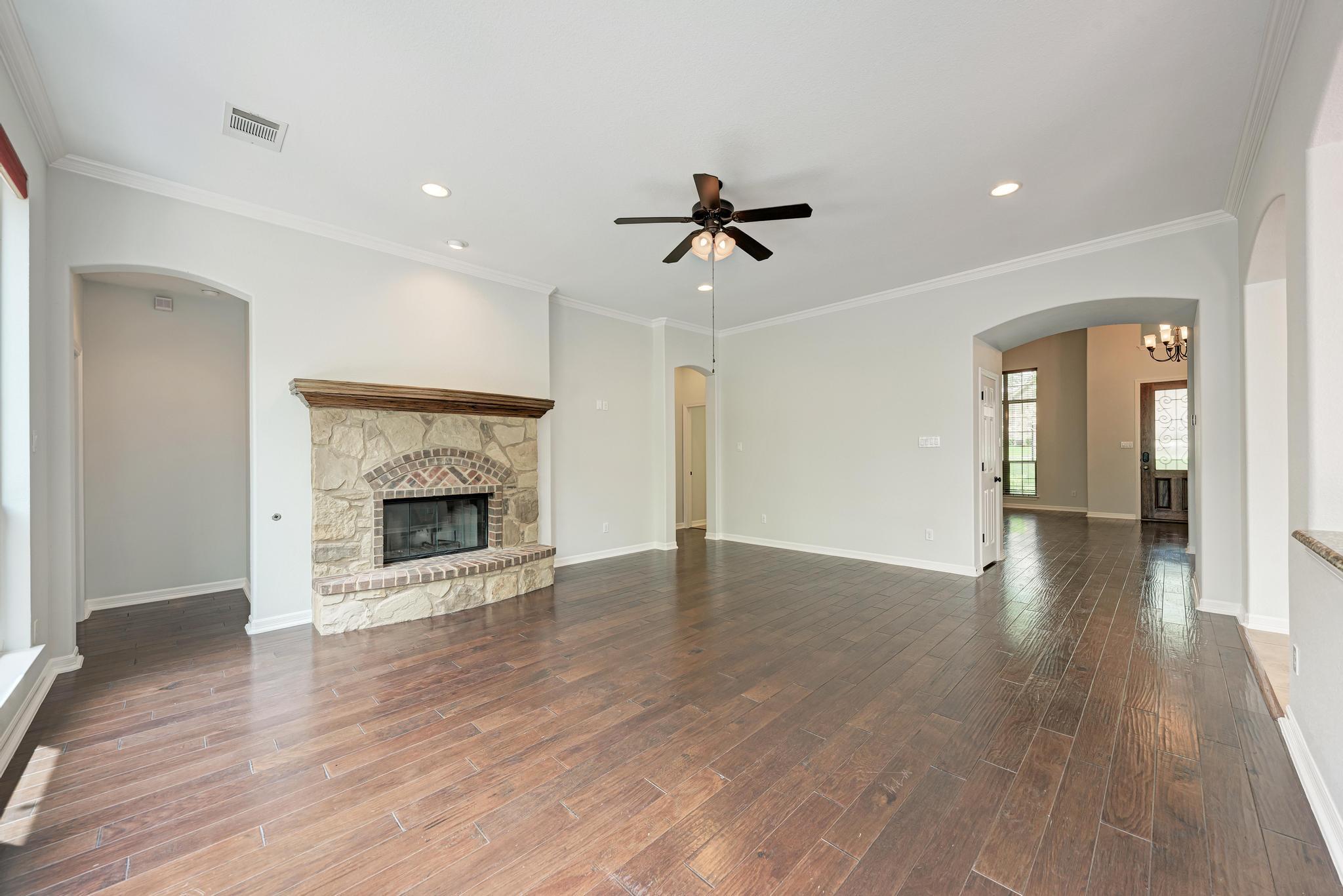 Unfurnished living room with a stone fireplace, dark plank flooring, and arched openings.