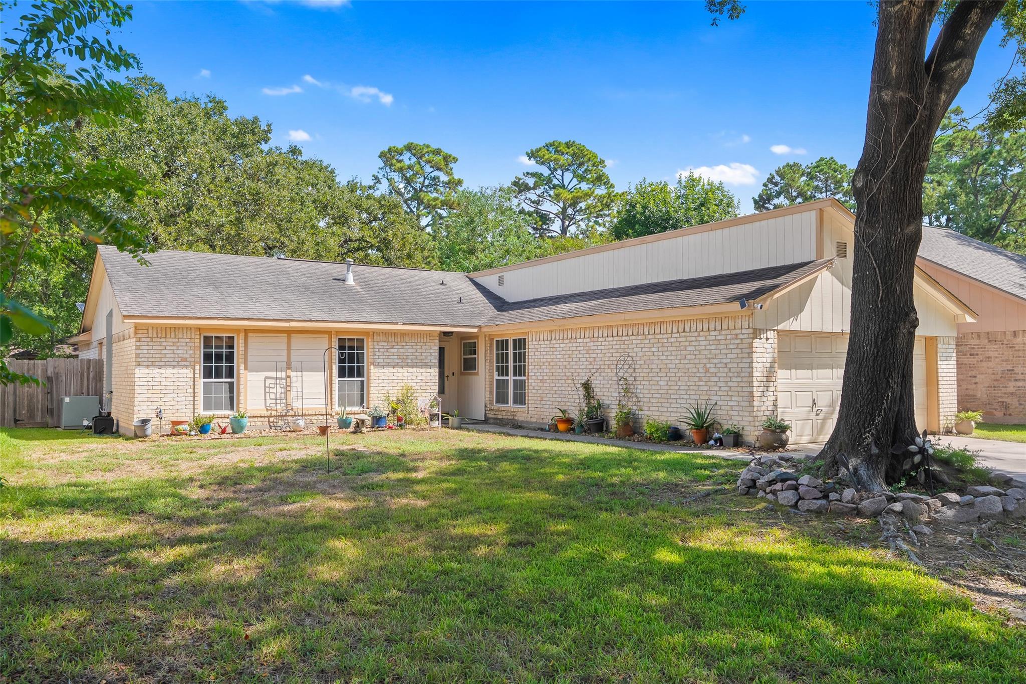 Single-story brick home with an attached garage, grassy front yard, and mature trees.