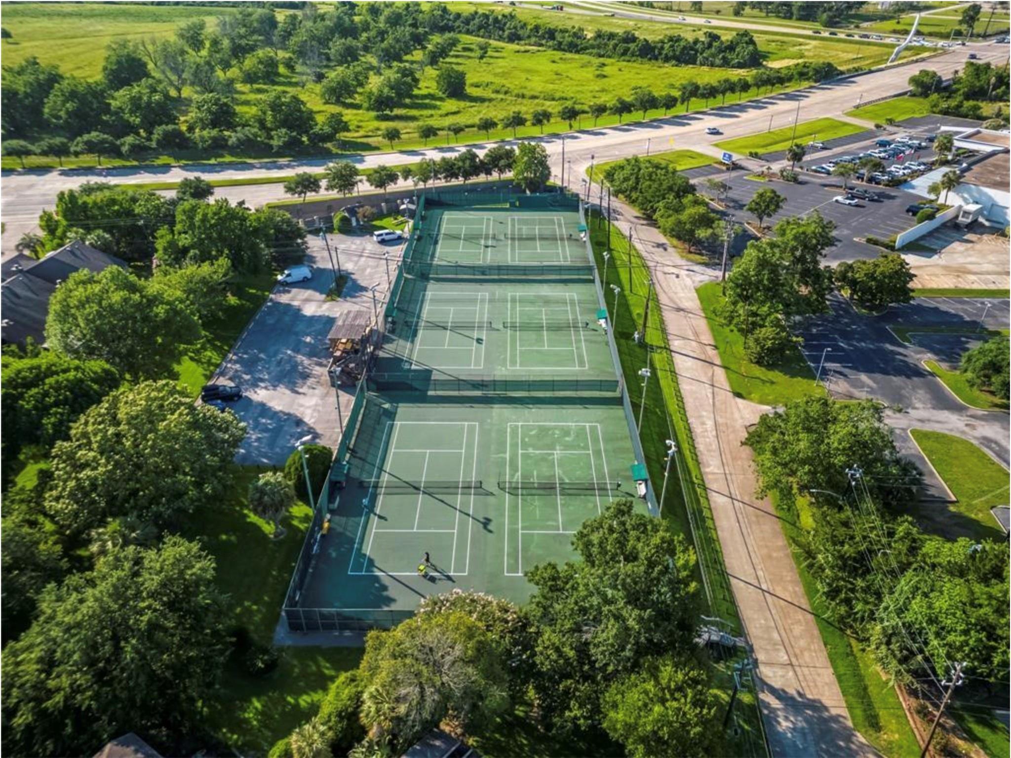 Three fenced tennis courts surrounded by trees, seen from above.