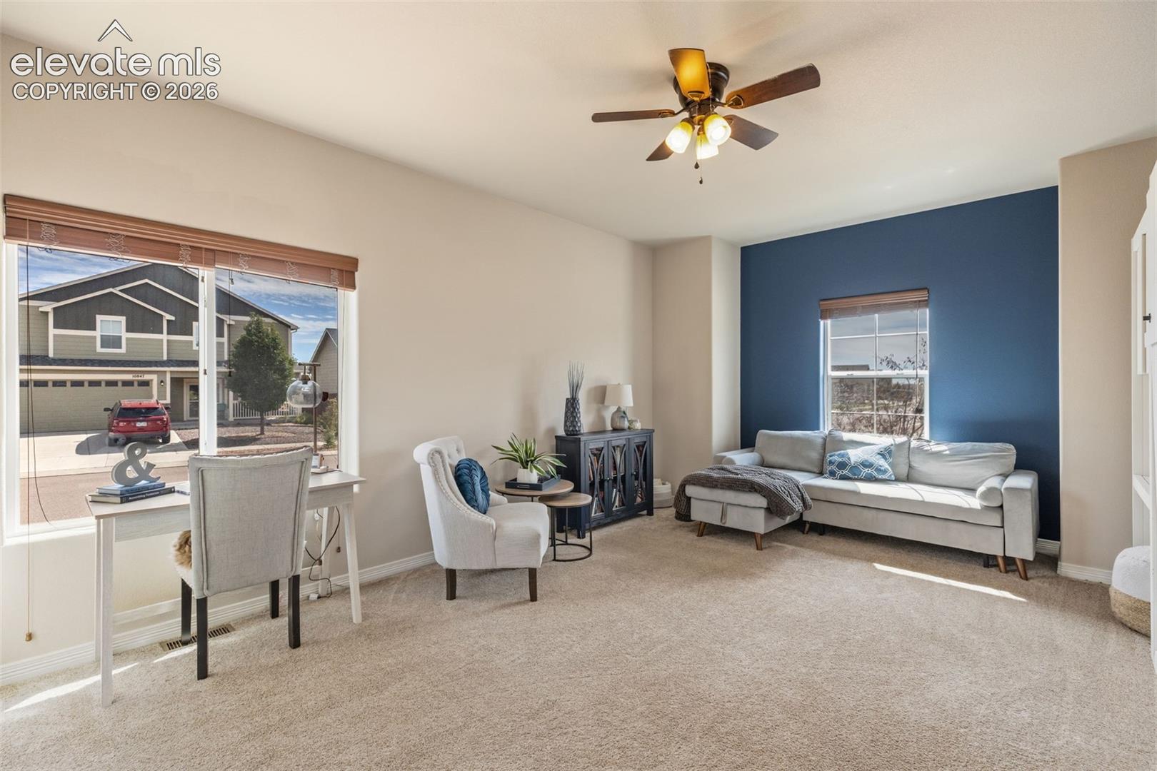 Living room with a blue accent wall, gray sectional, and desk beside large windows.