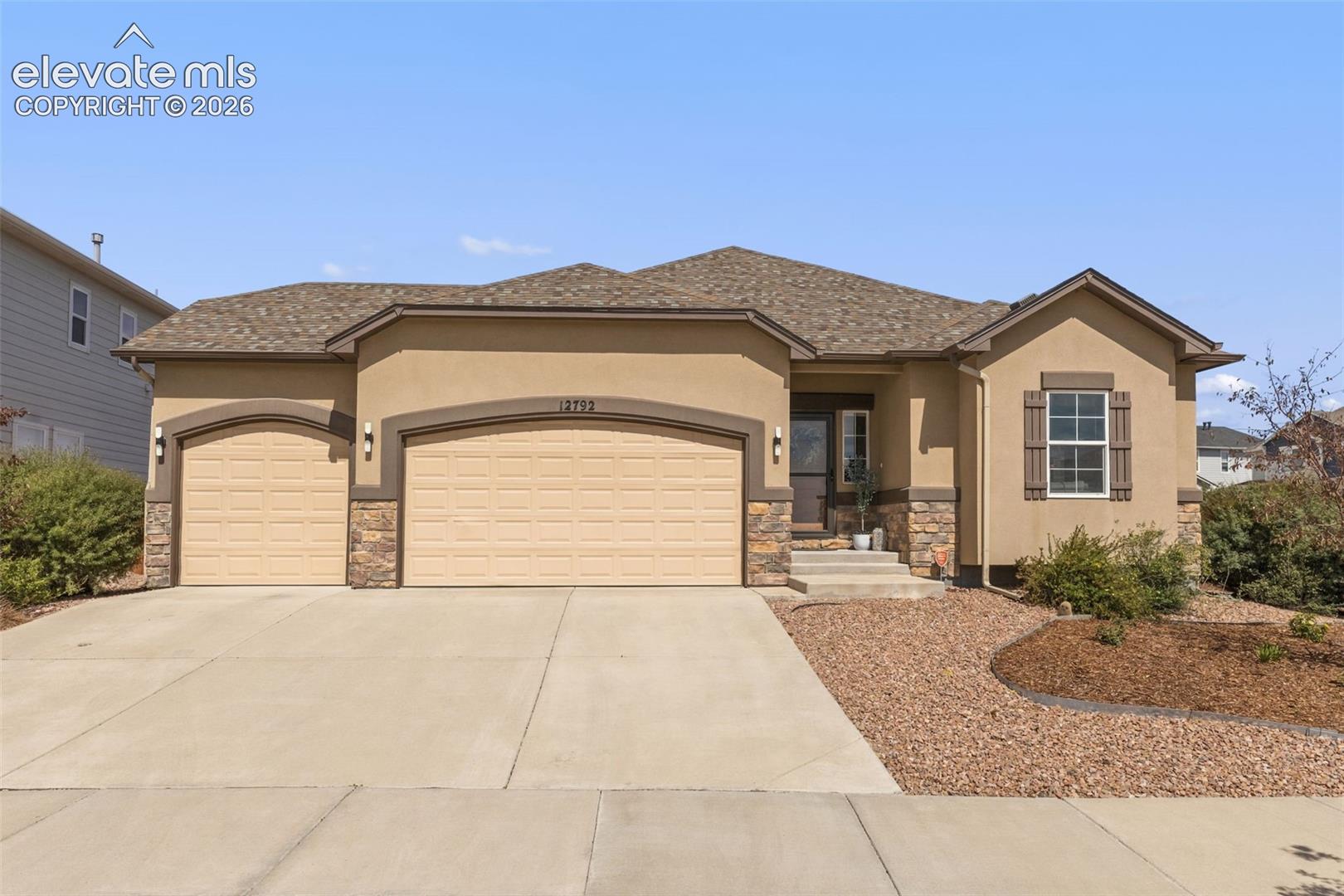 Tan single-story home with stone accents, three-car garage, and broad concrete driveway.