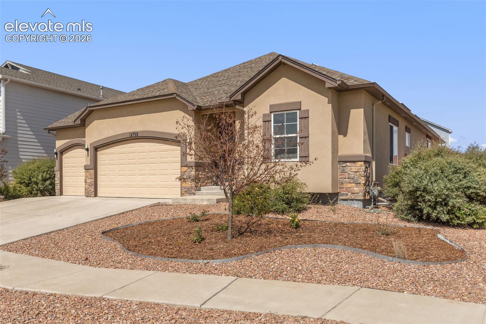 Tan stucco home with a stone-accented facade, two-car garage, and xeriscaped front yard.