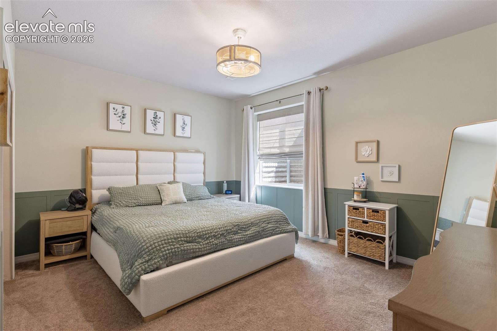 Furnished bedroom with a white upholstered bed, sage-green wall paneling, and a large window.