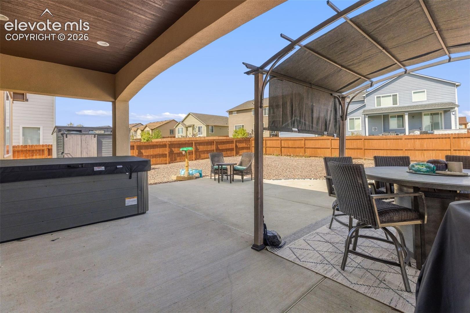 Covered backyard patio with a hot tub, pergola, and outdoor dining set.