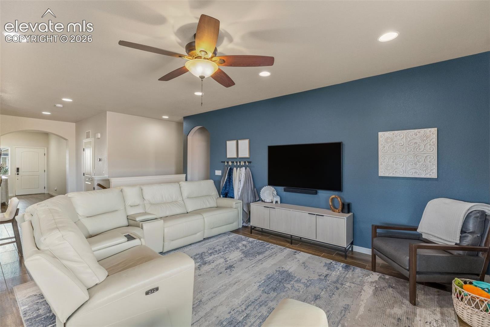 Living room with a white sectional, blue accent wall, and ceiling fan.