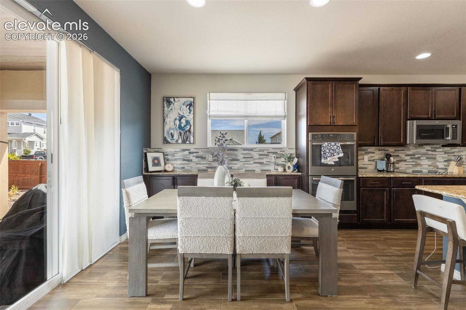 Kitchen and dining area with dark wood cabinets, a tiled backsplash, and a dining table beside sliding glass doors.