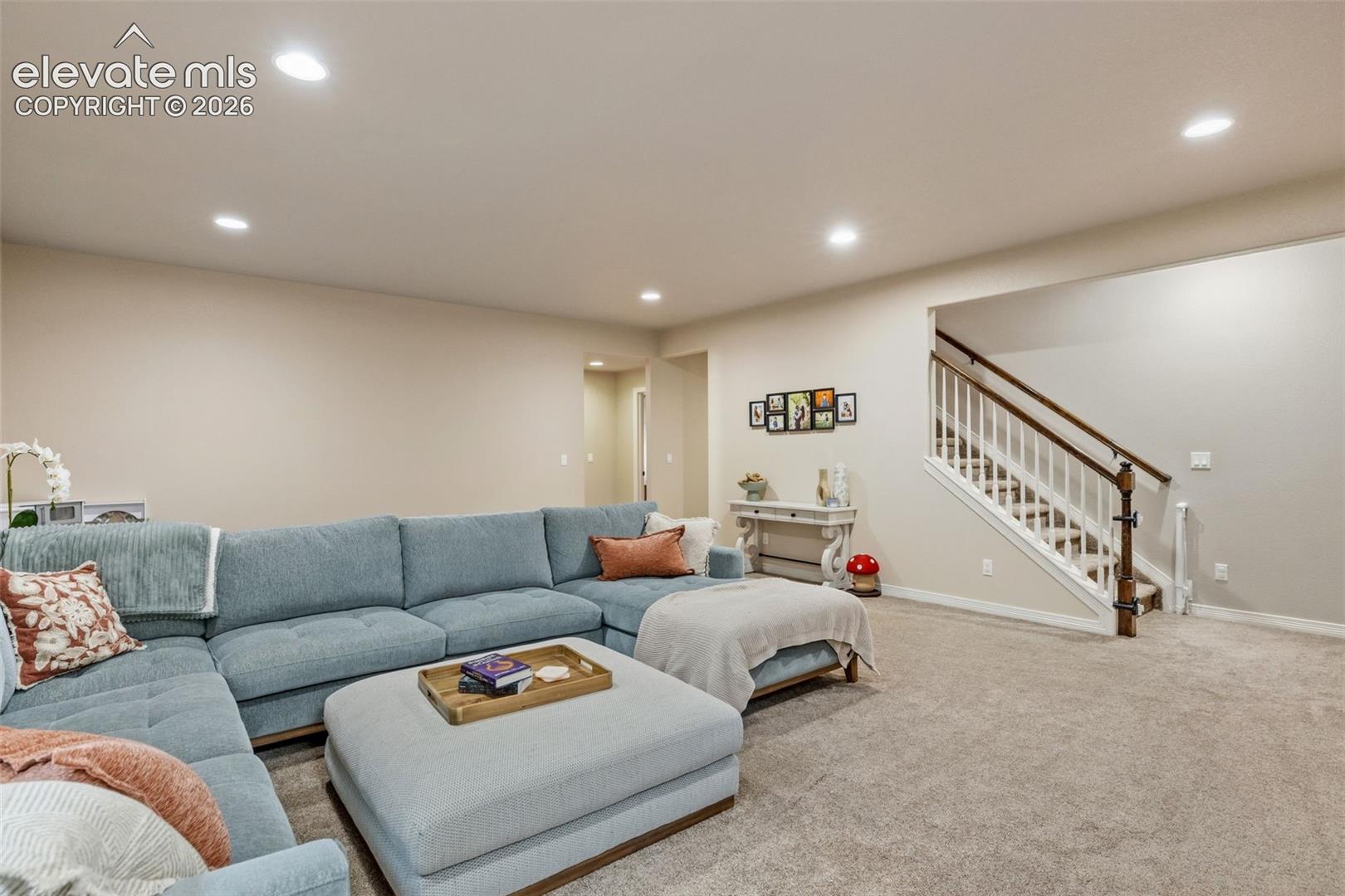 Furnished living room with a blue sectional sofa, large ottoman, and staircase.