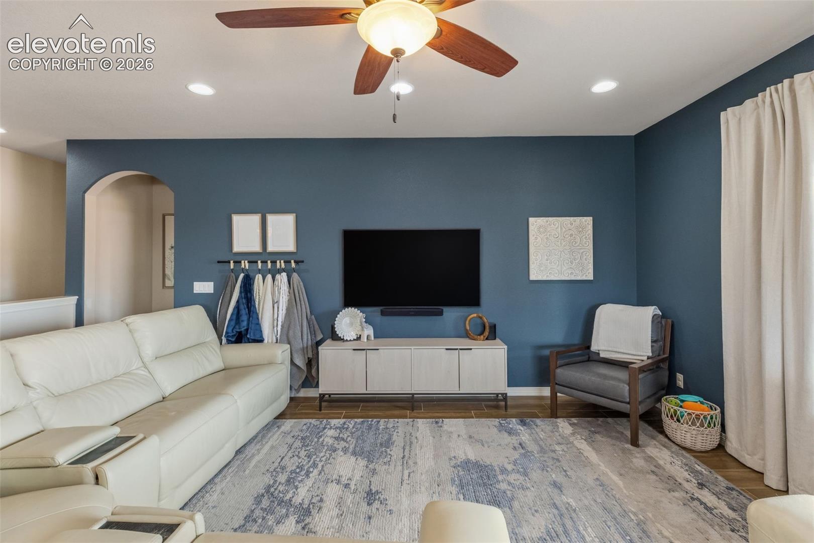 Living room with a blue accent wall, white sectional sofa, and ceiling fan.