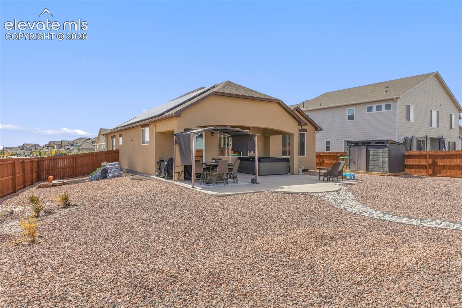 Home’s gravel backyard with solar panels, covered patio seating, and wooden fencing.