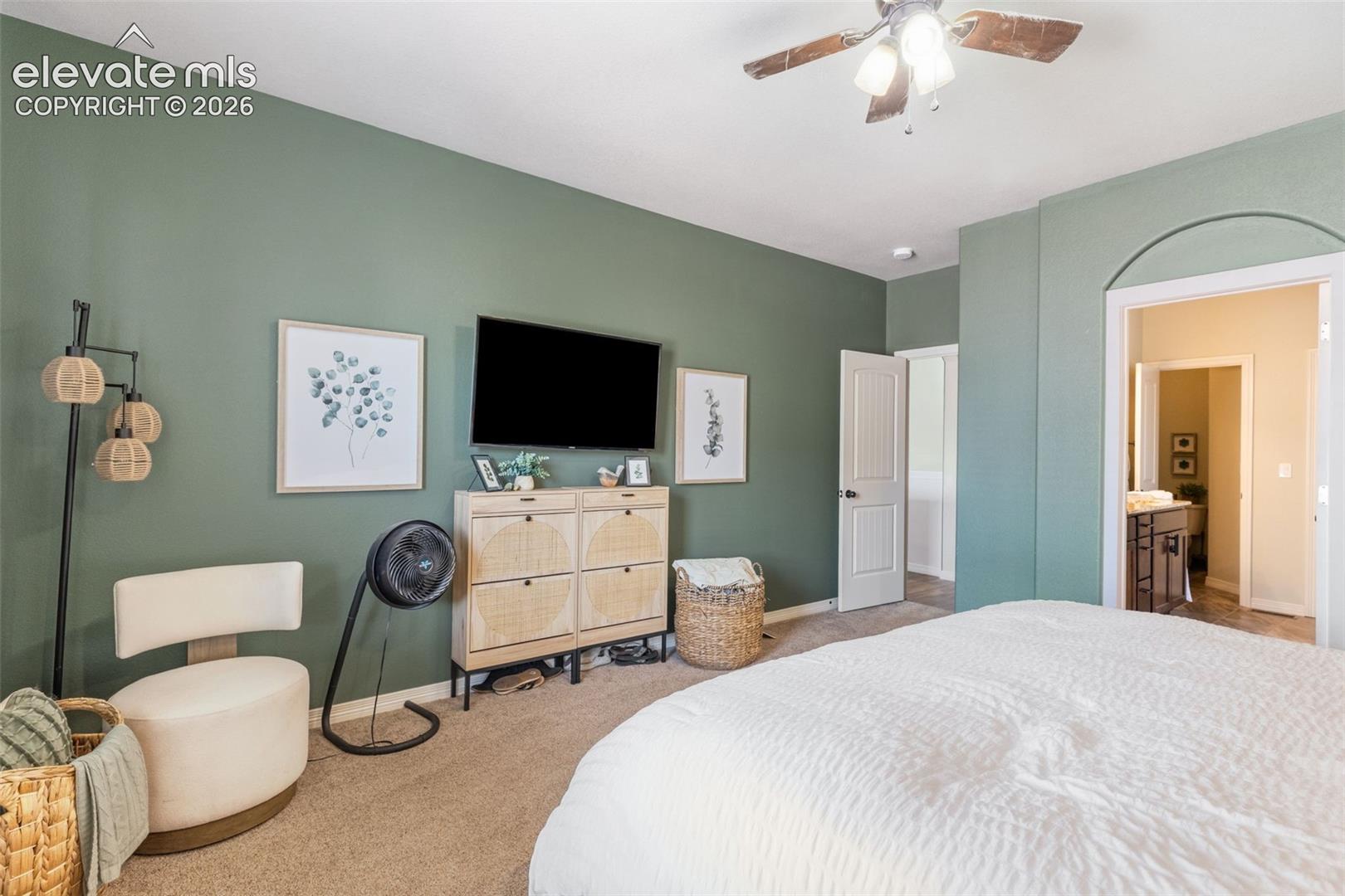 Bedroom with sage-green walls, a white bed, ceiling fan, and adjoining bathroom doorway.