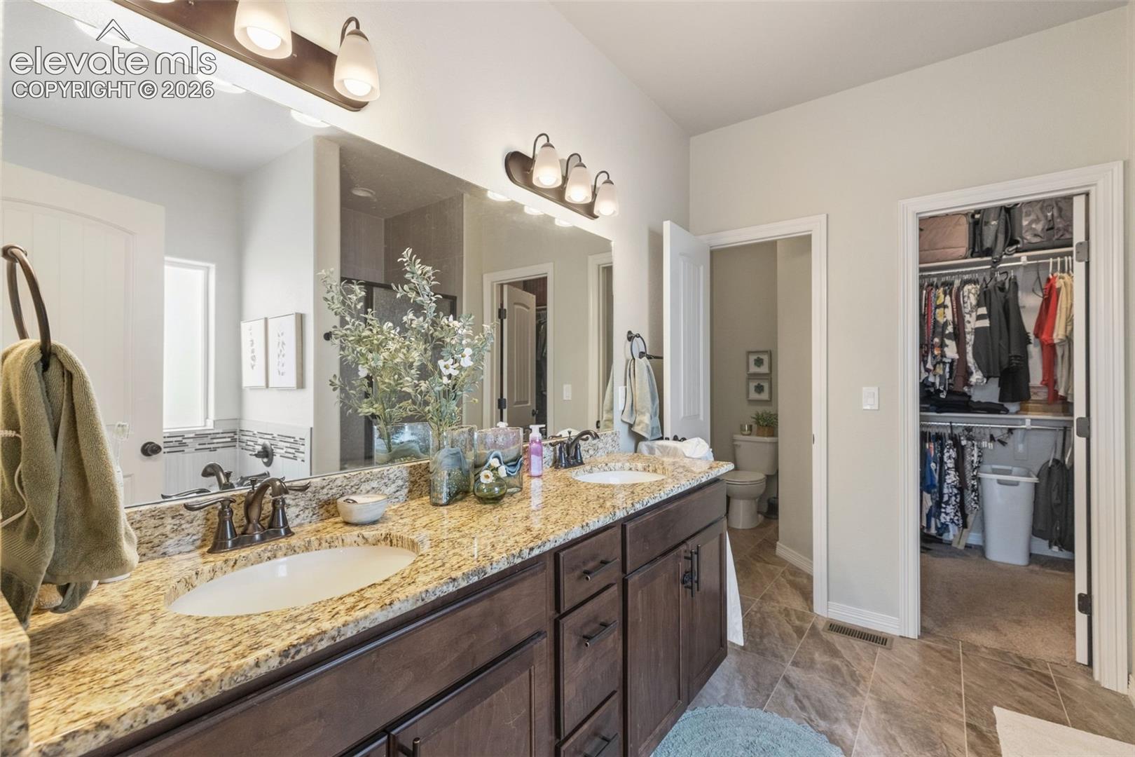 Bathroom with a double-sink vanity, granite countertop, and open walk-in closet.