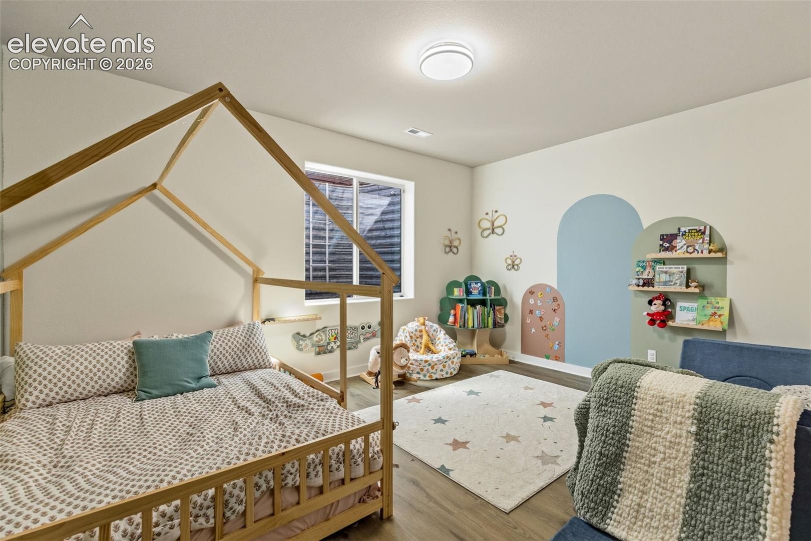 Children’s bedroom with a wooden house-frame bed, colorful arched wall niches, and book shelves.