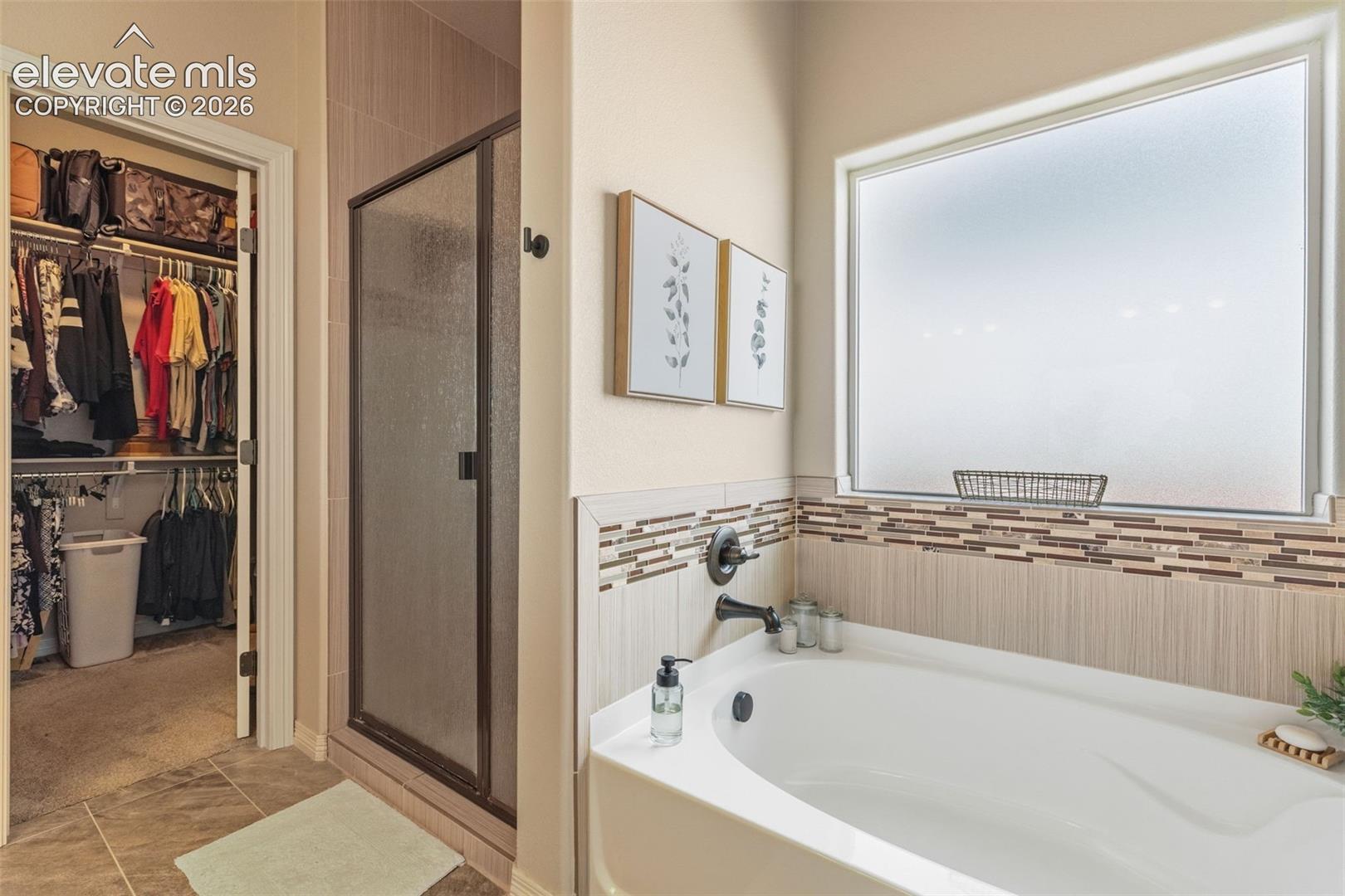 Bathroom with a white soaking tub, glass shower, and open walk-in closet.