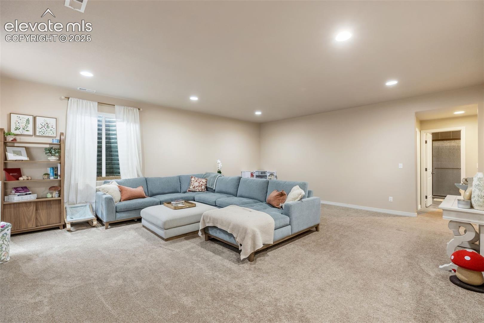 Carpeted living room with a blue sectional sofa, ottoman, and built-in shelving.
