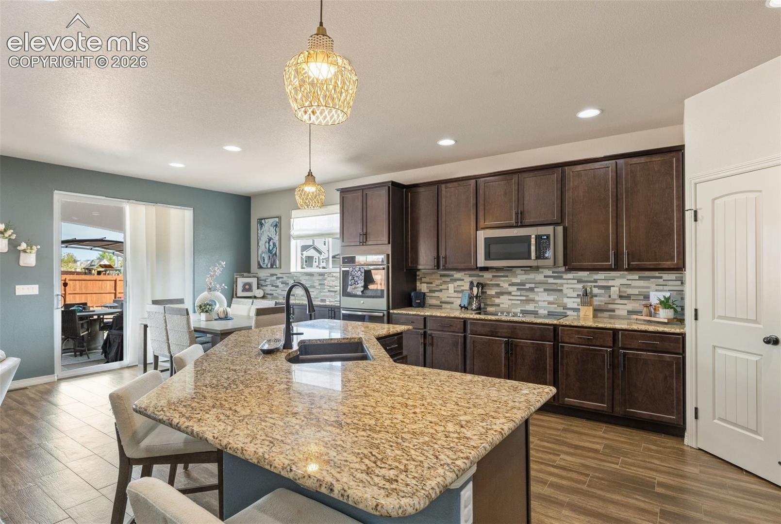 Kitchen with a granite island, dark wood cabinets, and two pendant lights.