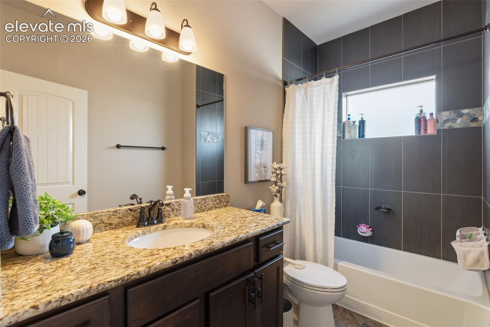 Bathroom with a granite vanity, dark tiled tub and shower, and a bright window.