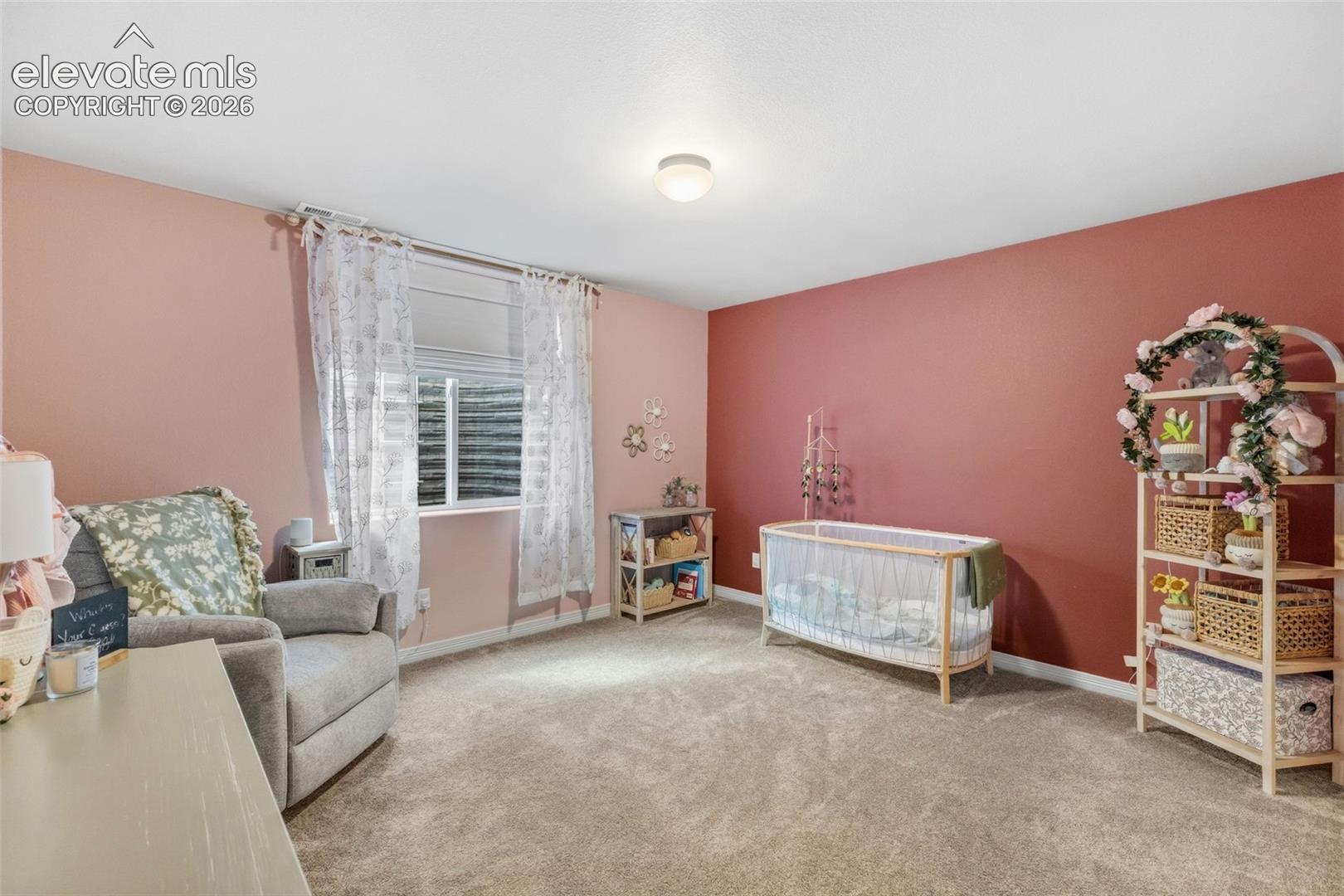 Nursery with a wooden crib, gray armchair, floral curtains, and pink accent wall.