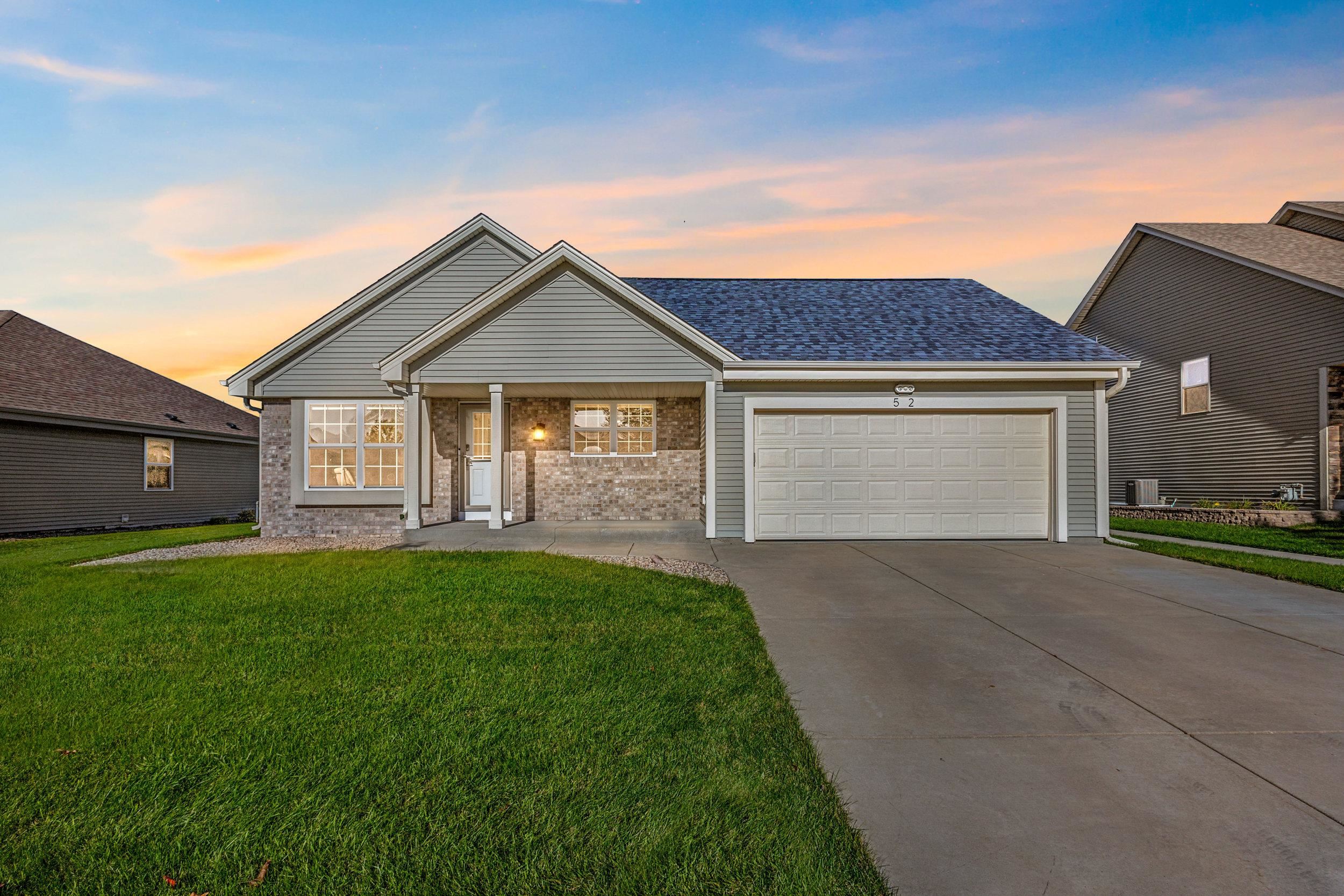 Suburban house with gray siding, brick accents, and a two-car garage at sunset.