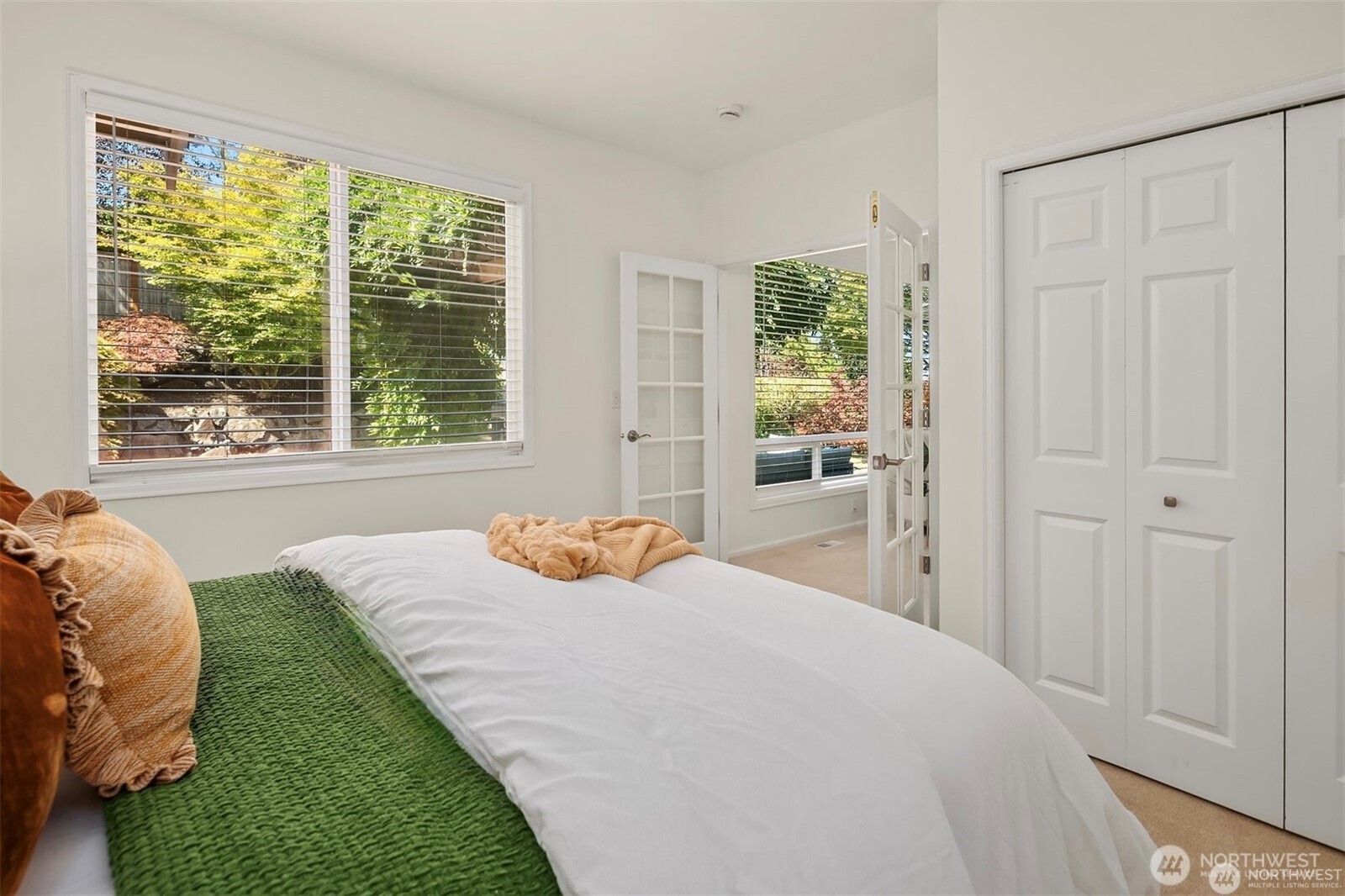 Bedroom with a green knitted blanket, wide windows, and white closet doors.