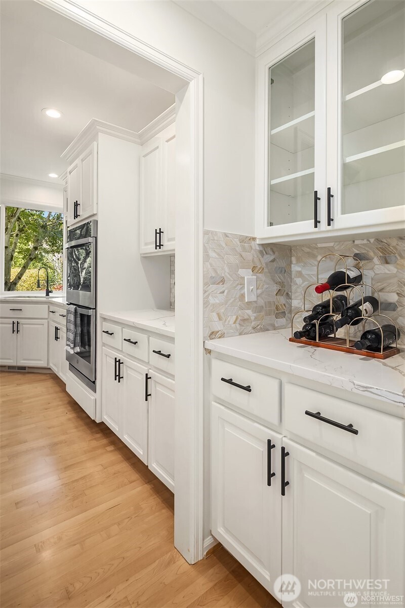White kitchen with a geometric tile backsplash, black cabinet pulls, and a countertop wine rack.