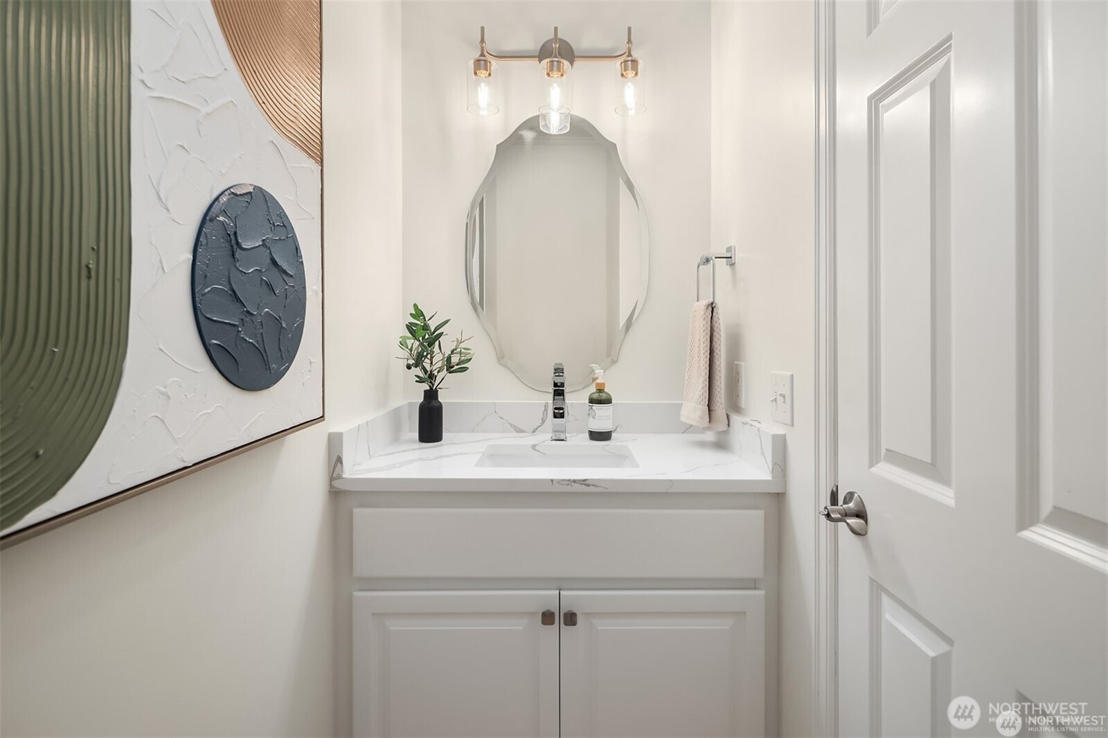 Bathroom vanity with marble-look counter, sculpted mirror, and brass lighting.