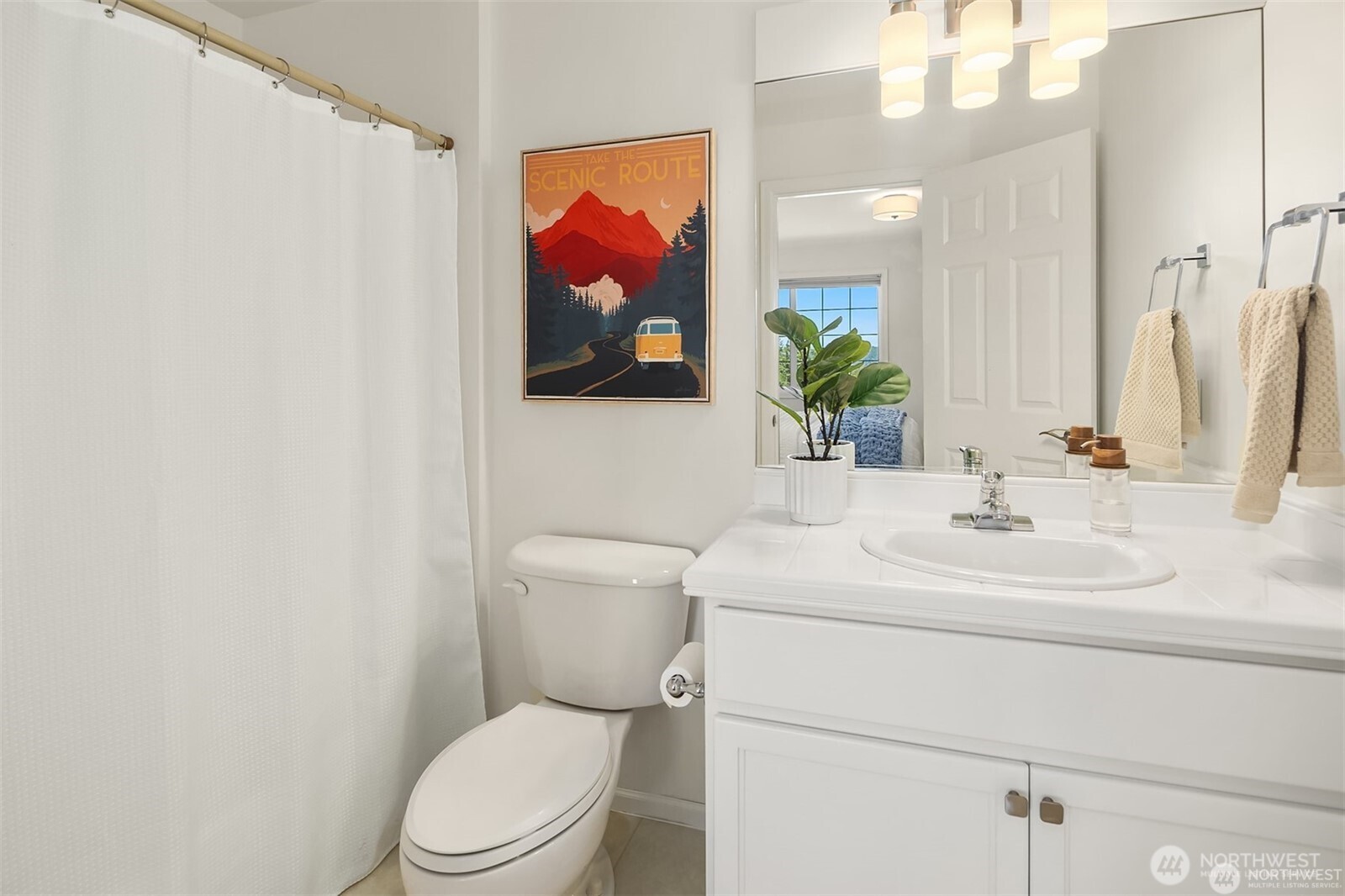 Bright bathroom with a white vanity, shower curtain, and framed scenic poster.