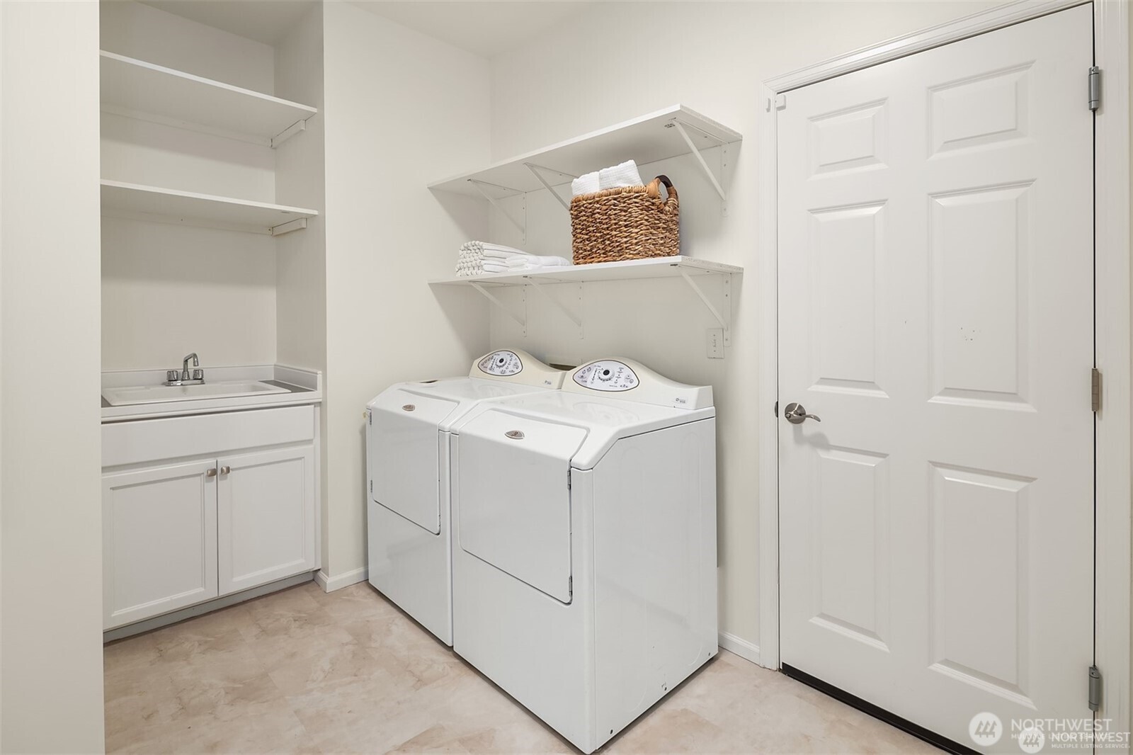 Laundry room with a white washer and dryer, utility sink, and open shelving.