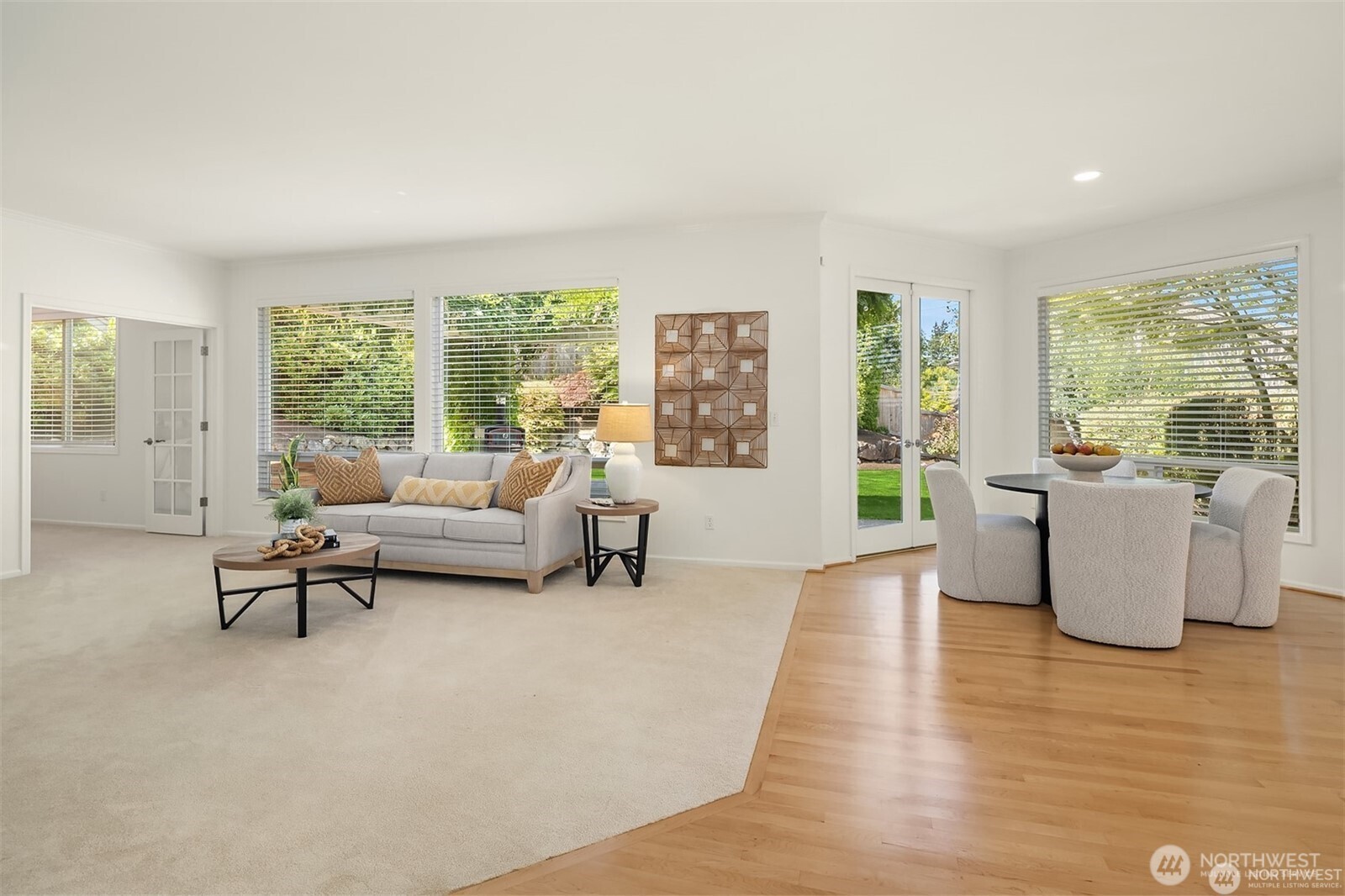 Staged living and dining area with a light sofa, large windows, French doors, and hardwood floors.