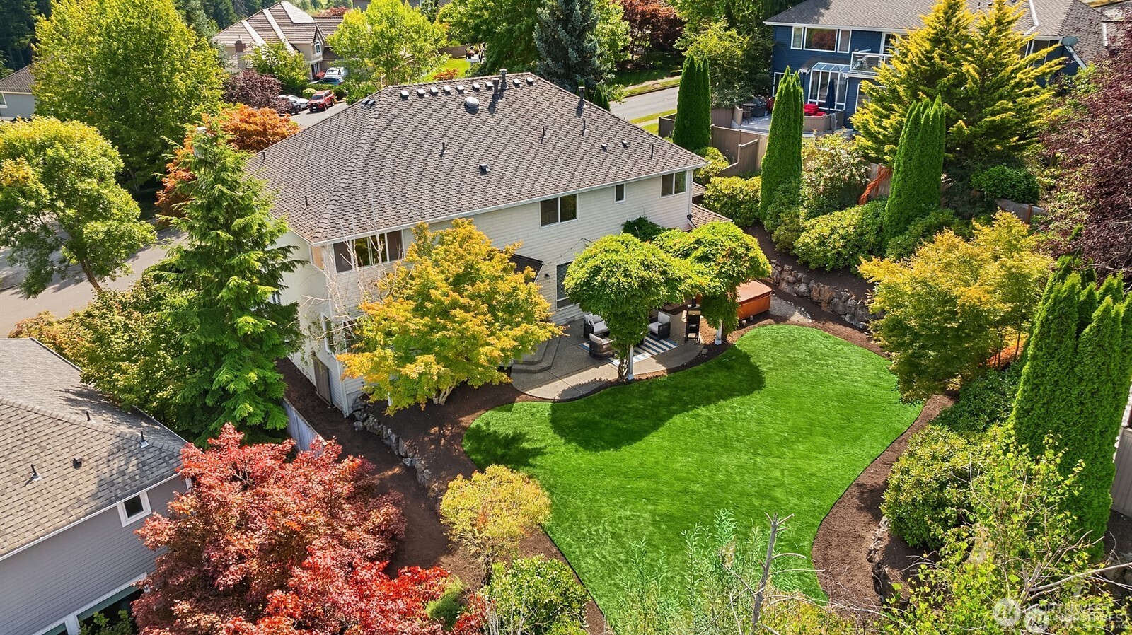 Aerial view of a home with a broad lawn, landscaped gardens, and a patio hot tub.