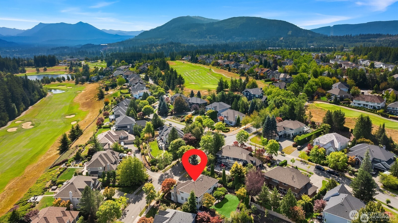 Aerial neighborhood view with the property marked in red beside a golf course and forested mountains.