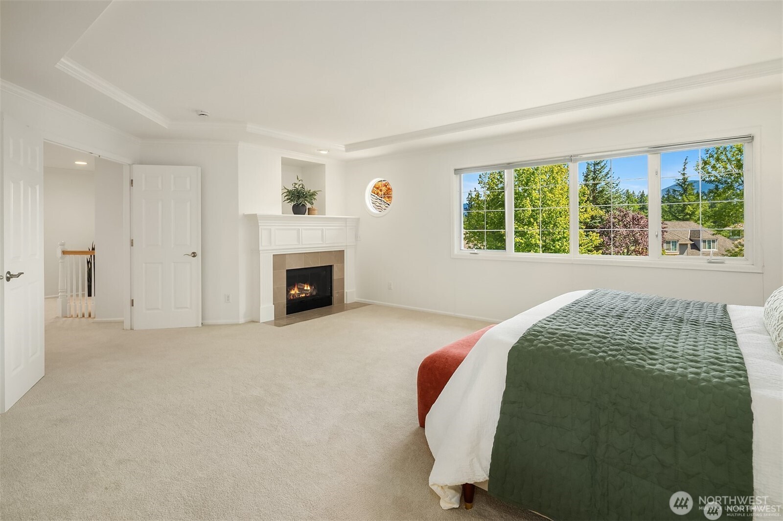 Bright bedroom with a green-quilted bed, large leafy outlook, and lit fireplace.