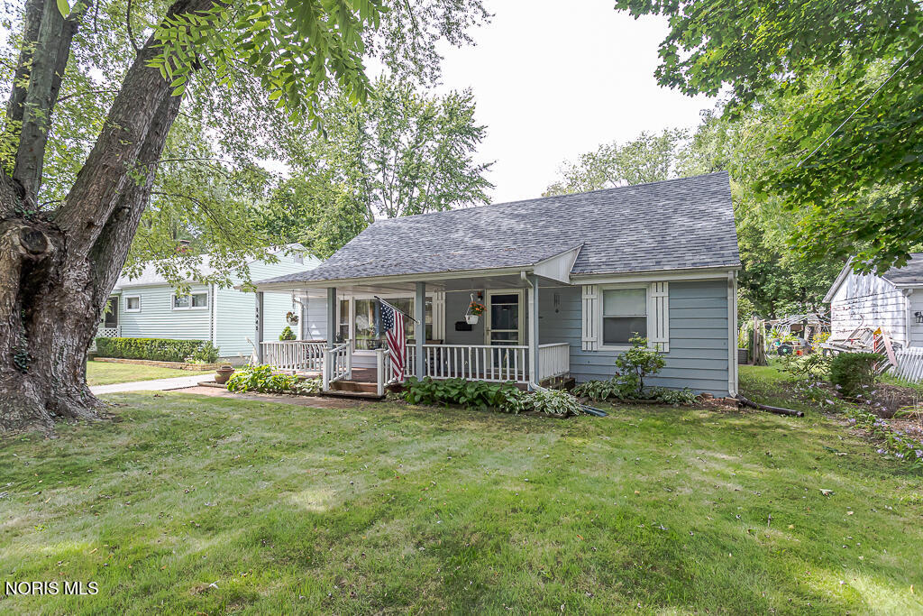 Light blue single-story home with a covered porch, shaded by mature trees.