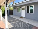 Paved patio beside a gray-sided home with white-trimmed windows and a covered area.