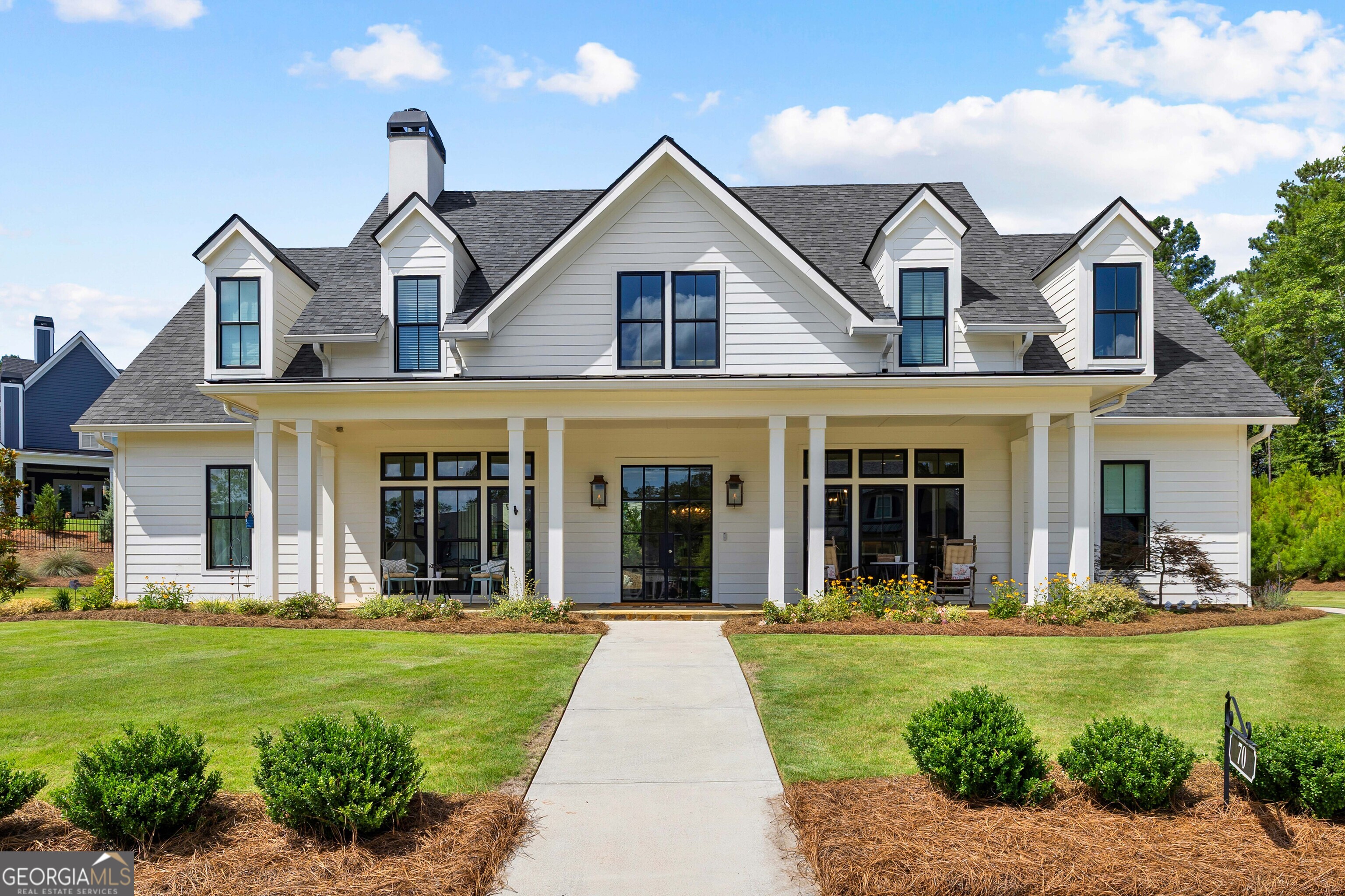 White two-story home with multiple dormers, a covered porch, and a walkway across the front lawn.