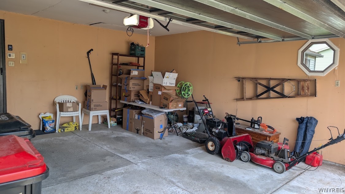 Garage with stacked boxes and lawn mowers beside the open overhead door.