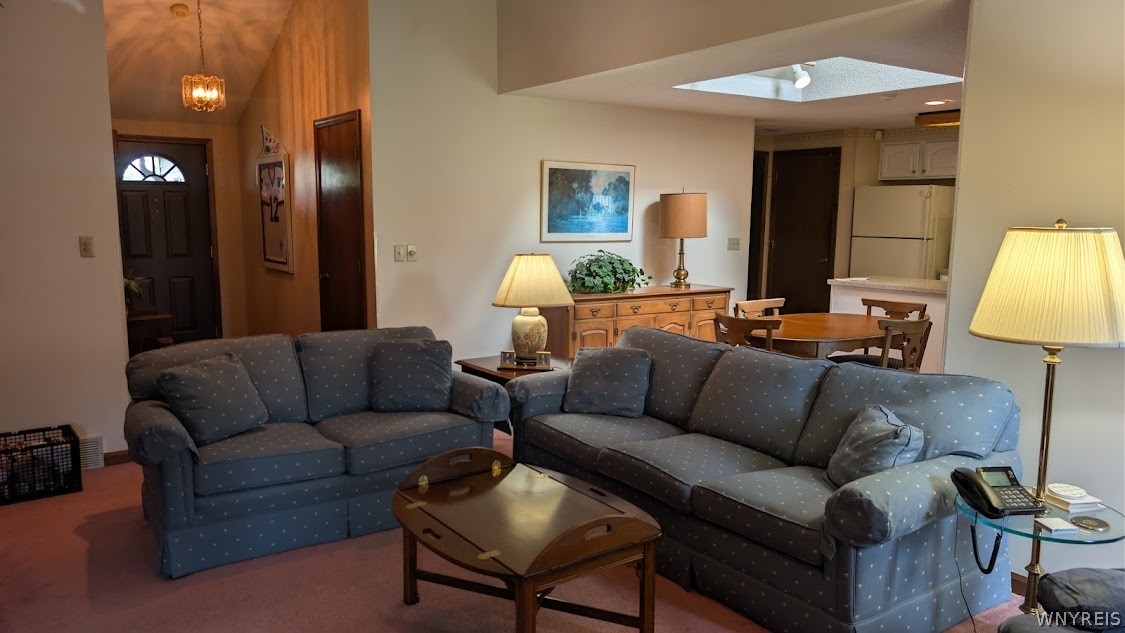Living room with two blue sofas, a wooden coffee table, and an adjoining dining area beneath a skylight.