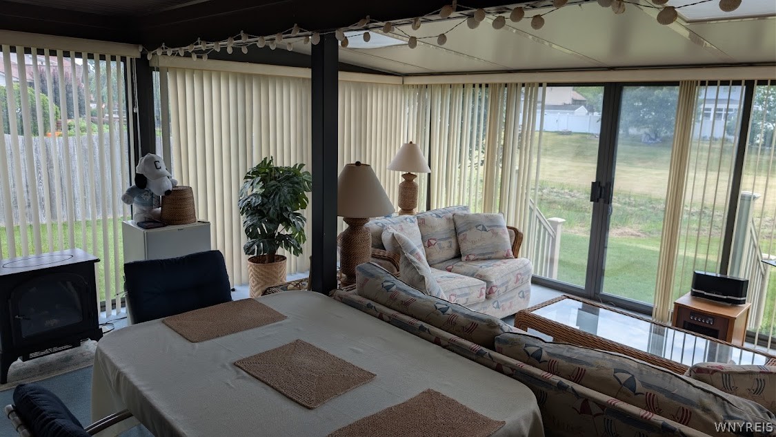 Furnished sunroom with a dining table, patterned sofas, and floor-to-ceiling windows overlooking a lawn.