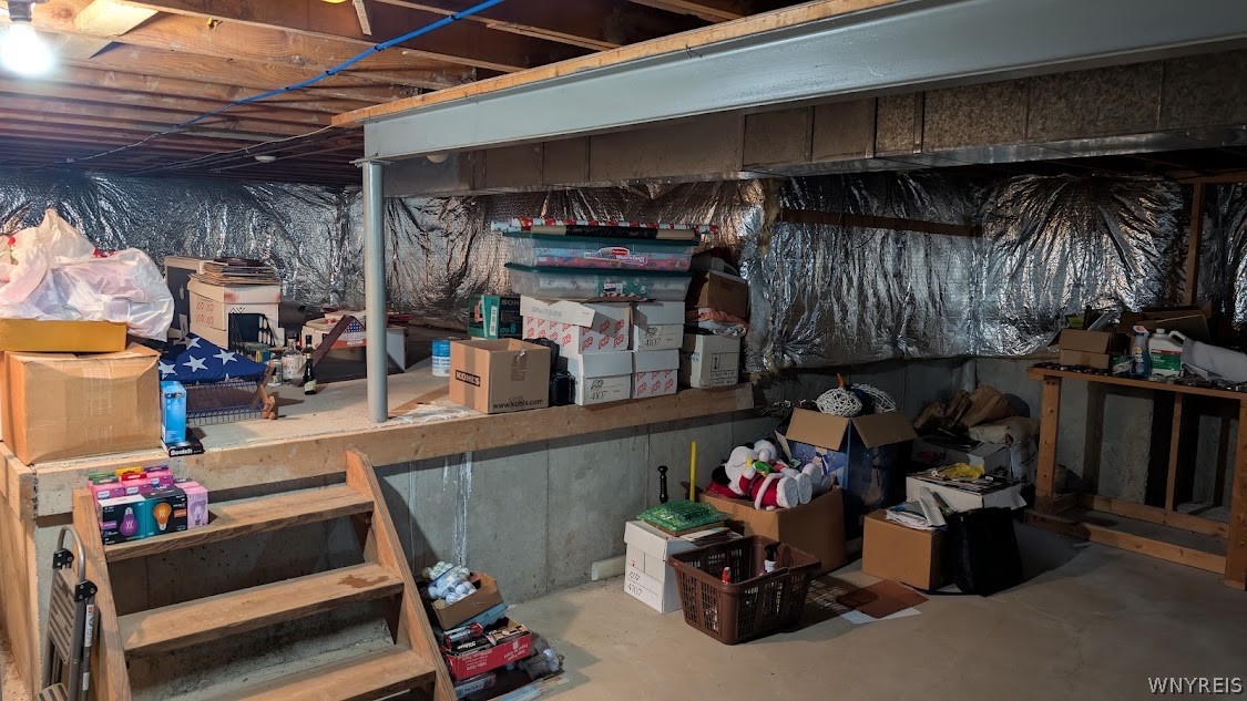 Unfinished basement storage area with a raised wooden platform, exposed joists, and boxes on the concrete floor.