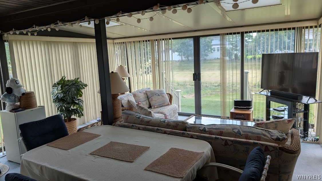 Furnished sunroom with a dining table, patterned sofas, and floor-to-ceiling windows overlooking the yard.