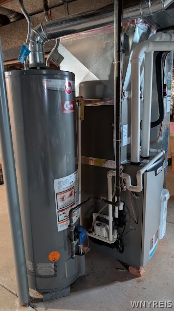 Basement mechanical area with a tall water heater, furnace, exposed pipes, and overhead ductwork.