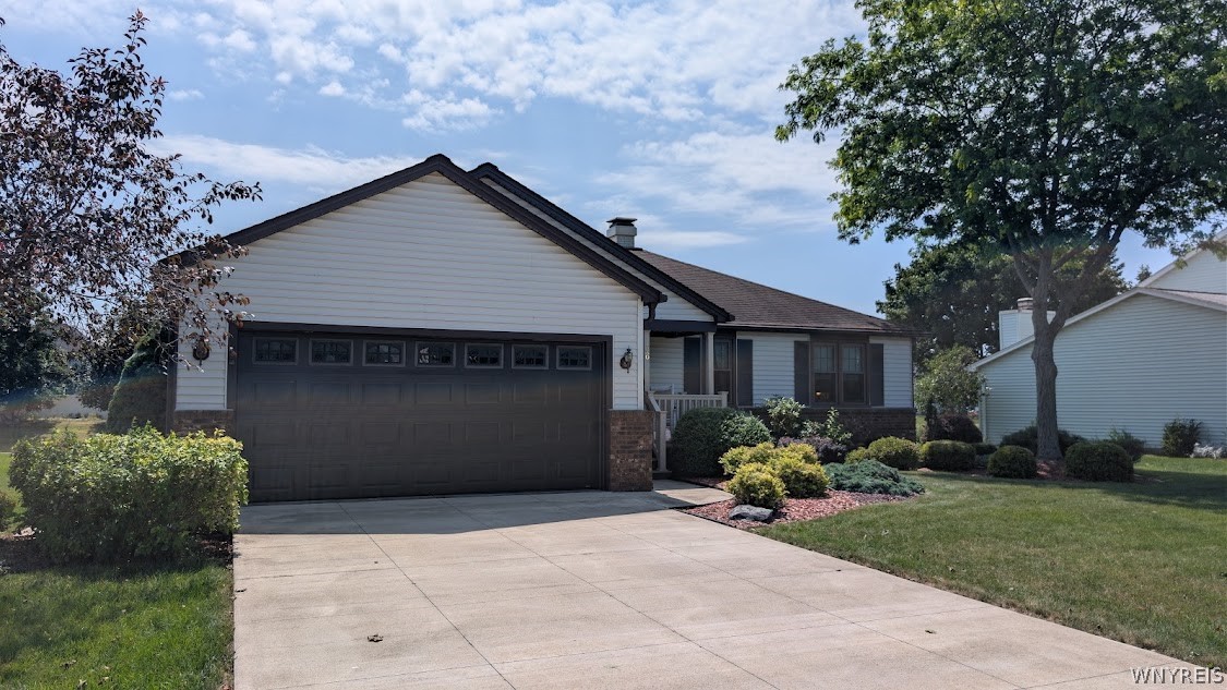 Single-story house with a dark double garage door, broad driveway, and landscaped front lawn.