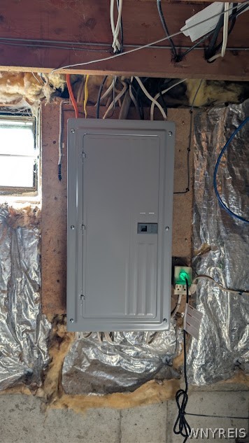 Electrical panel on exposed basement framing, surrounded by insulation and visible wiring.